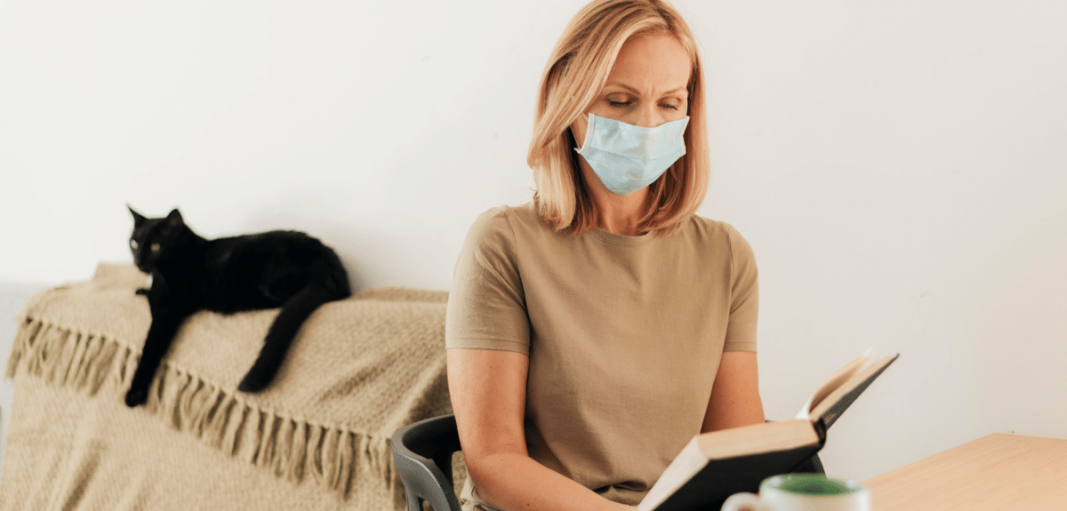 Femme avec masque médical à la maison avec lecture de chat pendant la quarantaine